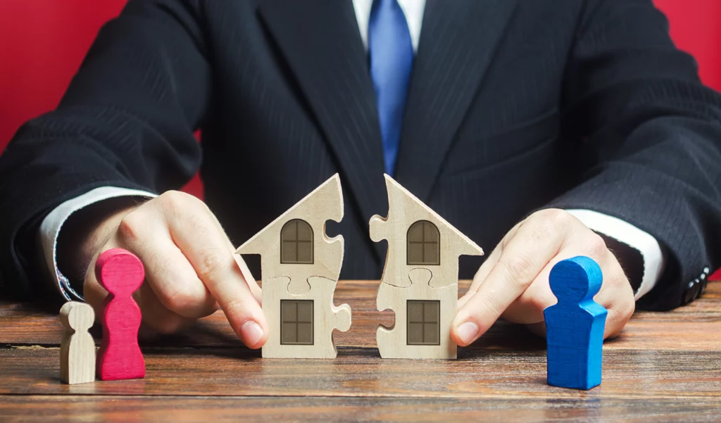 Person holding split house puzzle with figures, symbolizing property division in divorce.