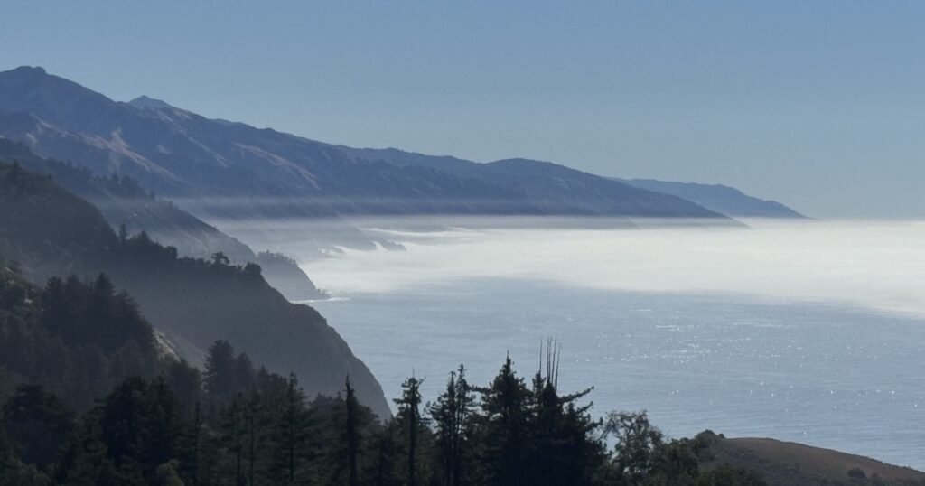 Fog rolling over the Big Sur coastline below forested ridges